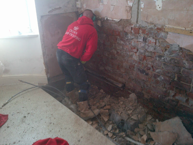 An operative in a red Crown Damp-Proofing hoodie hacking off contaminated plaster